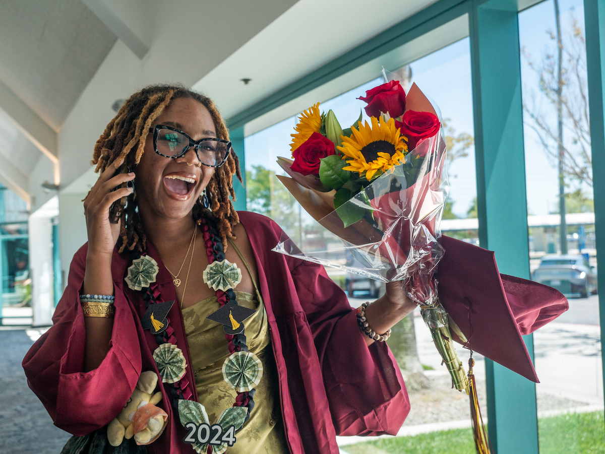 young woman in grad cap with flowers and phone