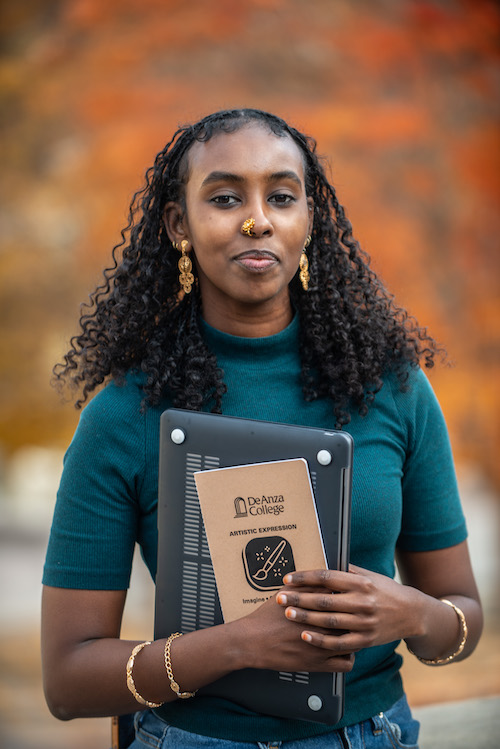 young woman holding laptop and booklet titled "De Anza College"