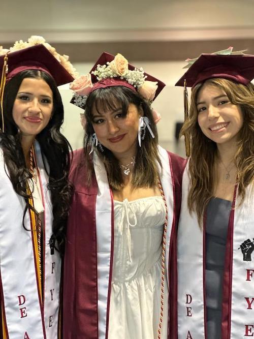 three young women in grad gowns and caps with flowers